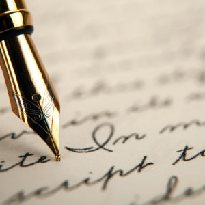A fountain pen nib is touching a piece of paper that has handwritten words in cursive.