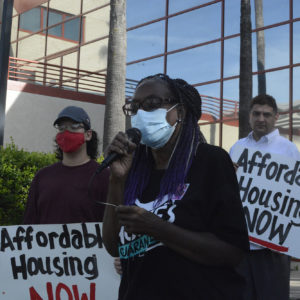 Elyse Gittens addresses the crowd outside Merced Civic Center while two community members stand behind her both holding signs that say "AFFORDABLE HOUSING NOW"