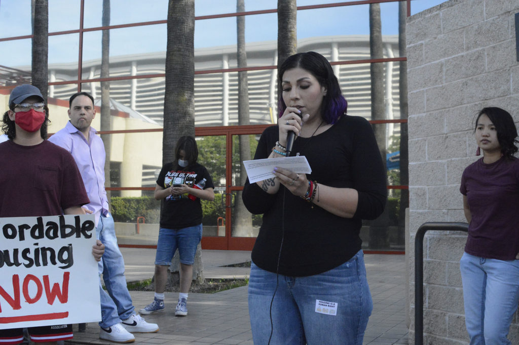 Jazmin Moreno stands in front of Merced Civic Center, holding a microphone and reading from notes.