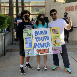 Three young people hold up a sign together that says "Build Youth Power Today"